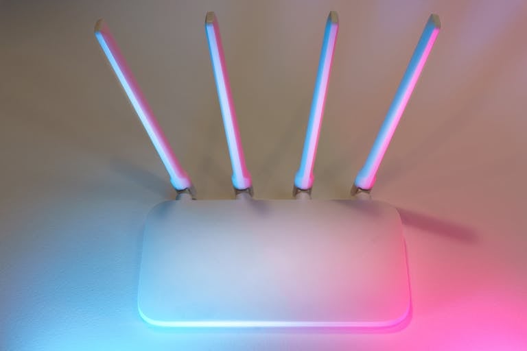 Sleek white wireless router with four antennas emitting soft blue and pink light.